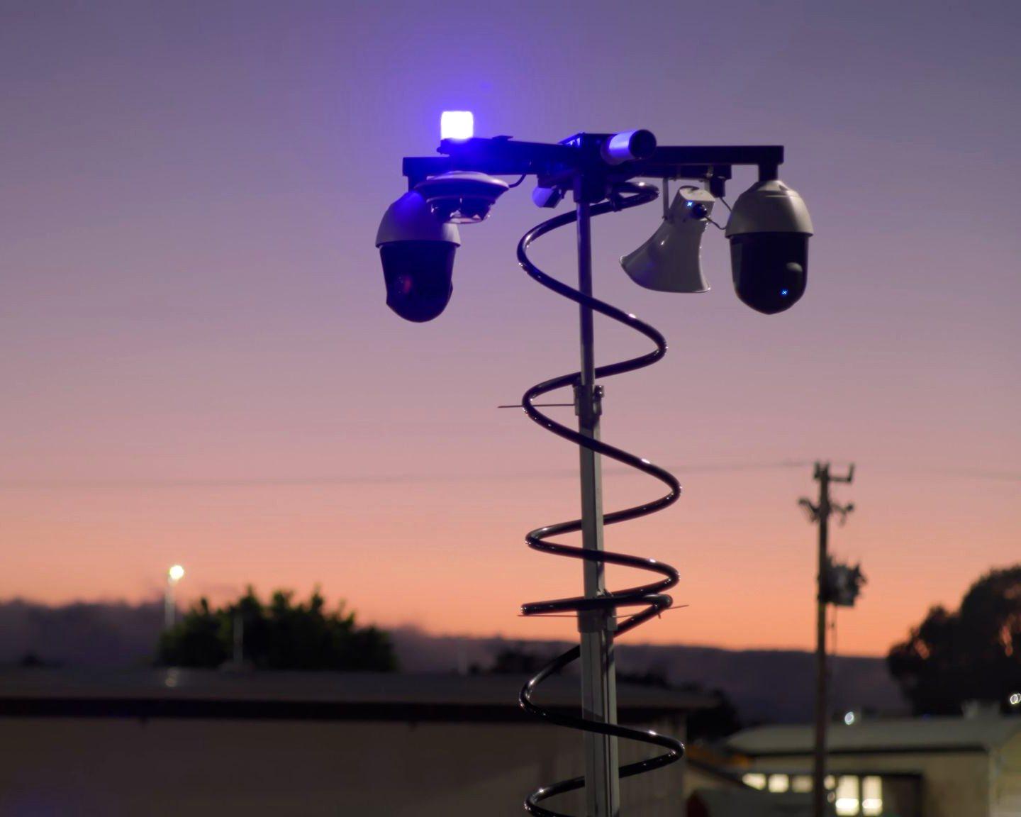 Verkada MT81 security trailer mast head at dusk — PTZ cameras, talk-down horn speaker, and blue LED beacon on the telescoping mast